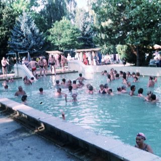 Busy outdoor swimming pool with many people enjoying water.