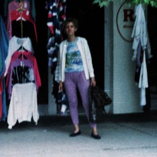 Outdoor clothing stall with colorful garments displayed. Woman walking by.