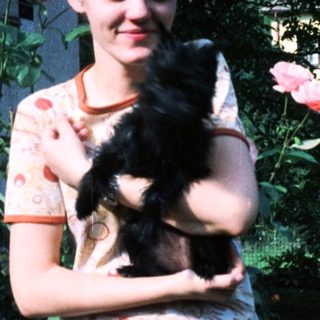 Woman holding black cat amid blooming roses.