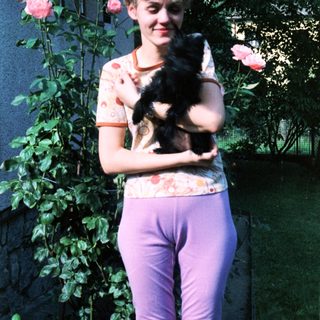 Woman holding black cat amid blooming roses.