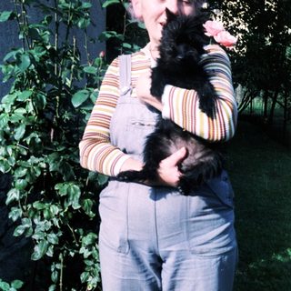 Woman holding black cat amid blooming roses.