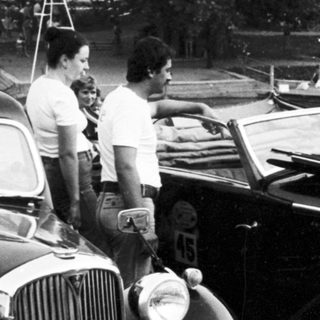 Classic cars and people at outdoor gathering.
