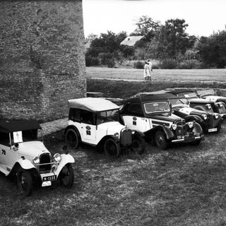 Vintage cars parked near historic stone wall.