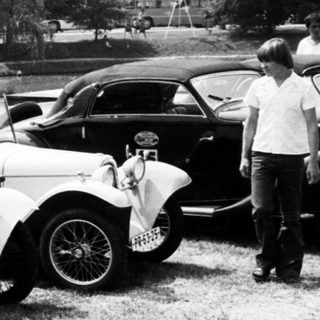 Classic vintage cars parked outdoors in grassy area.
