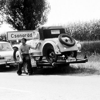 Classic cars being towed on rural road near Csornárad sign.