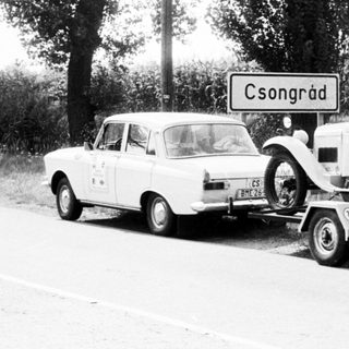 Vintage car being towed behind modern vehicle on road.