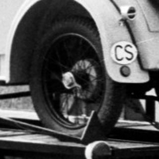 Vintage car being towed behind modern vehicle on road.