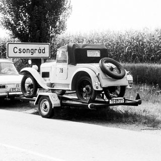 Vintage car being towed behind modern vehicle on road.