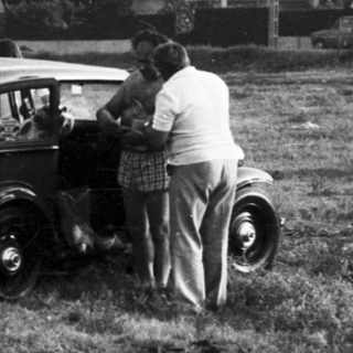 Vintage cars parked in grassy field with people.