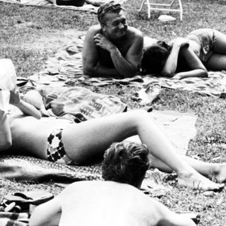 People relaxing on grass by a poolside.