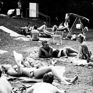 People relaxing on grass by a poolside.