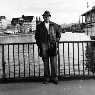 Man in vintage attire posing by waterfront.