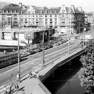 Urban street scene with tram, bridge, and mid-century buildings.