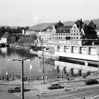 Historic waterfront cityscape with buildings, boats, and street.