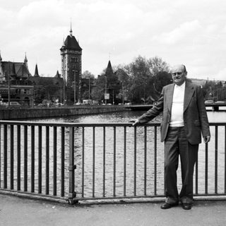 Man standing by river railing in urban setting.