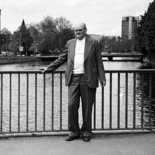 Man standing by river railing in urban setting.