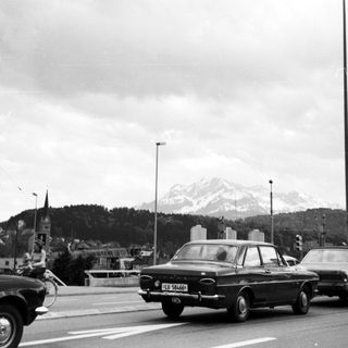 Vintage cars on urban highway near snowy mountain.