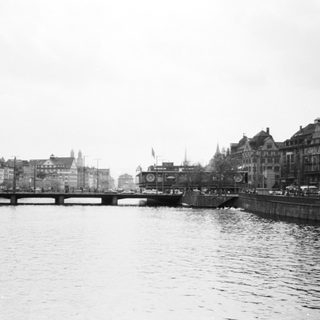 Black-and-white cityscape with river bridge and historic buildings.