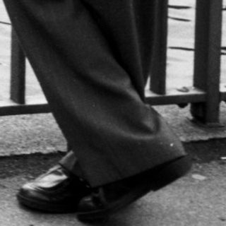 Man in 1950s attire stands by river.