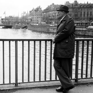 Man in 1950s attire stands by river.