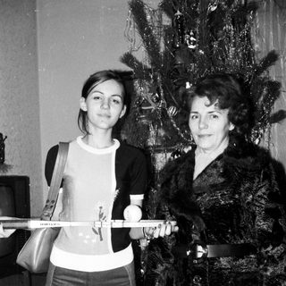 Two women posing with a ski pole indoors near a Christmas tree.