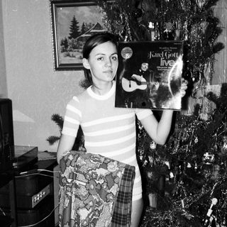 Young woman holding a record album near a Christmas tree.