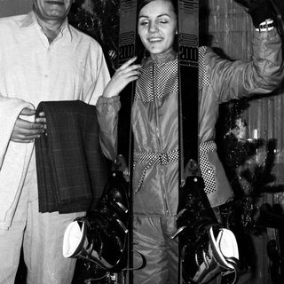 Two people posing with skis indoors.