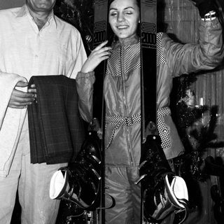 Two people posing with skis indoors.