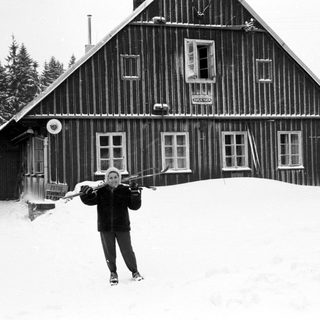Person skiing in front of snowy wooden cabin.