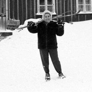 Person skiing in front of snowy wooden cabin.