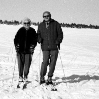 Two people cross-country skiing on snow-covered terrain.