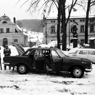 Snowy street scene with vintage car and people.