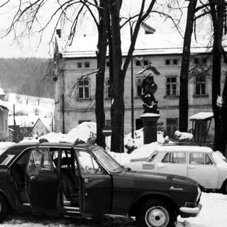 Snowy street scene with vintage car and people.