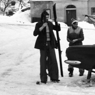 Snowy street scene with vintage car and people.