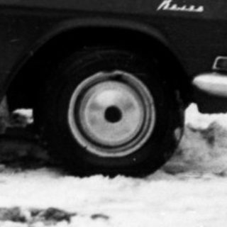 Snowy street scene with vintage car and people.