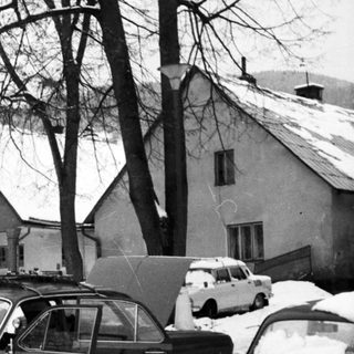 Snowy street scene with vintage cars and people clearing snow.