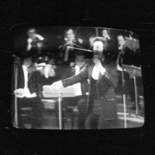 Black-and-white concert scene with conductor leading orchestra.