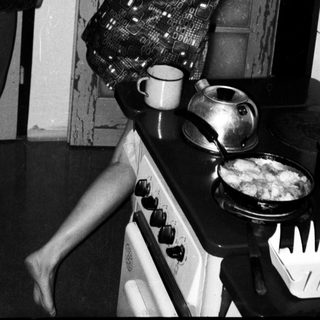 Two women playing a playful game near a stove.