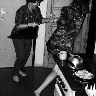 Two women playing a playful game near a stove.