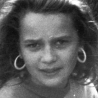 Young girl smiling near rough wall.