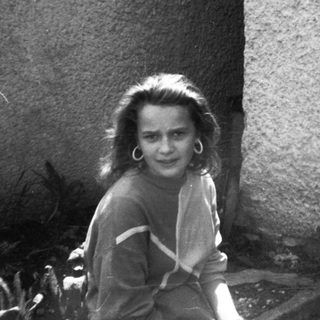 Young girl smiling near rough wall.