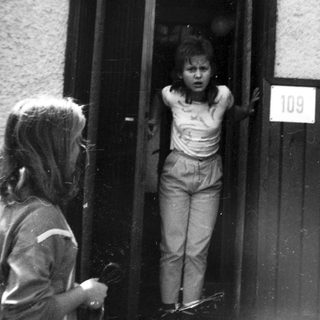 Two children at apartment door, one peeking out.