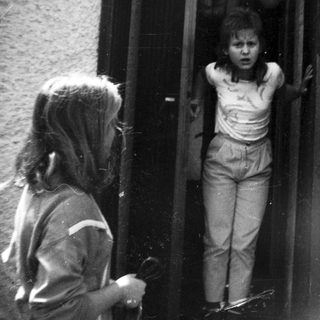 Two children at apartment door, one peeking out.