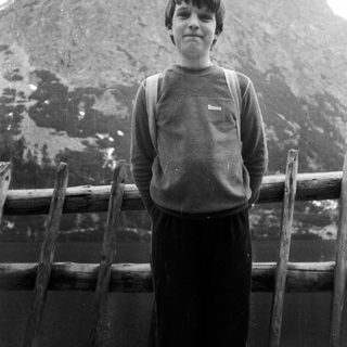 Boy standing near snowy mountain with wooden railing.