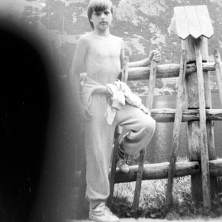 Shirtless boy sitting on rustic wooden fence.