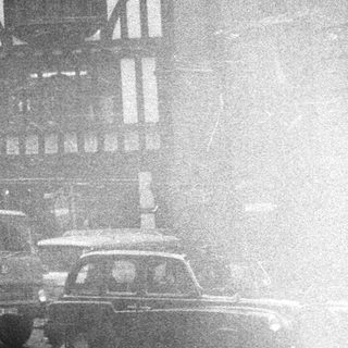 Black-and-white street scene with Tudor-style buildings and vintage cars.