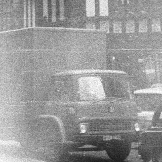 Black-and-white street scene with Tudor-style buildings and vintage cars.