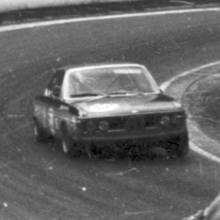 Race car driving on curved track. Spectators watching.