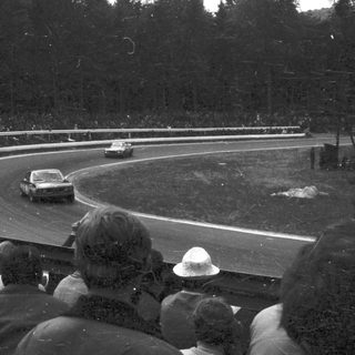 Race car driving on curved track. Spectators watching.