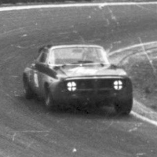 Classic race car on wet track during nighttime event.